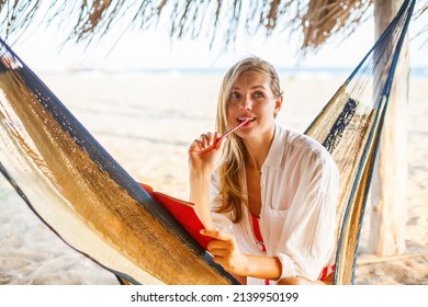 Beautiful blonde woman writing something in her red planner sitting in a hammock on a beach. Life or job planning in comfortable environment. - Powered by Shutterstock