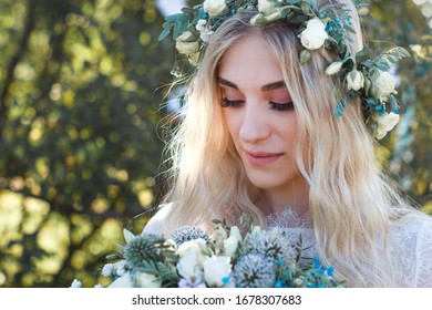 Beautiful Blonde Young Bride Portrait With Flower Bouquet And Wreath On Her Head In White Wedding Dress Outdoor In Summer