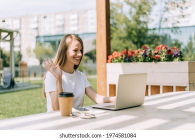 Beautiful Blonde Young Woman Having A Video Chat At Laptop, Sit Down On Bench Outside In Public Park. Happy Student Lady Girl In White T-shirt Distance Learning, Education, Work And Online Shopping.