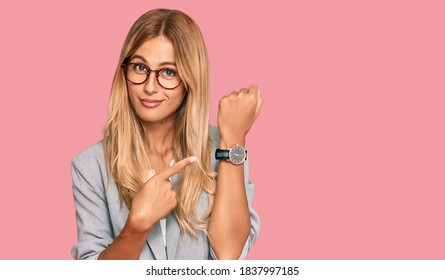 Beautiful blonde young woman wearing business clothes in hurry pointing to watch time, impatience, looking at the camera with relaxed expression 