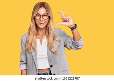 Beautiful blonde young woman wearing business clothes smiling and confident gesturing with hand doing small size sign with fingers looking and the camera. measure concept. 