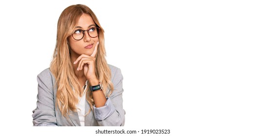 Beautiful blonde young woman wearing business clothes with hand on chin thinking about question, pensive expression. smiling with thoughtful face. doubt concept.  - Shutterstock ID 1919023523