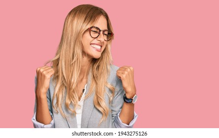 Beautiful blonde young woman wearing business clothes very happy and excited doing winner gesture with arms raised, smiling and screaming for success. celebration concept. 