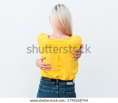 Beautiful blonde young woman wearing yellow shirt hugging oneself happy and positive from backwards. self love and self care