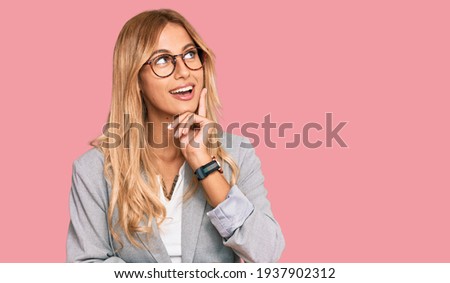 Beautiful blonde young woman wearing business clothes with hand on chin thinking about question, pensive expression. smiling and thoughtful face. doubt concept. 