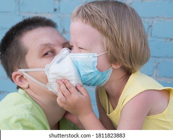 Beautiful Blond-haired Child In Protective Medical Mask Hugs And Kisses His Mother. Bald Extravagant Woman In Green Coat And Quarantine Medical Mask, Blue Gloves