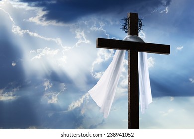 Beautiful blue sky with clouds and sunbeams shining on a cross for Easter morning. The cross includes burial cloth and crown of thorns.