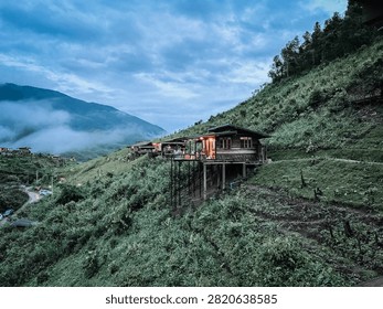 Beautiful blue sky with dramatic clouds above lush green mountains and rolling hills covered by morning mist. Scenic mountain landscape featuring a peaceful countryside resort in northern Thailand
