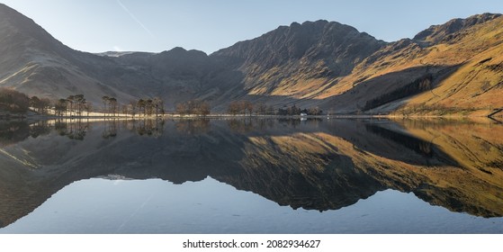 Beautiful blue sky and mirrored reflections in lake with mountains catching golden morning light. Buttermere, Lake District, UK. British scenic views. Travel and holiday destinations.