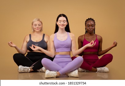 Beautiful body positive women of different size and appearances meditating together indoors, young happy multiethnic females in sportswear sitting in lotus pose with eyes closed over beige background - Powered by Shutterstock