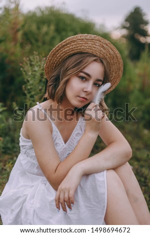 beautiful boho girl sitting at sunset light near lake. attractive young woman in white bohemian dress with windy hair relaxing near water among green leaves. summer vacation