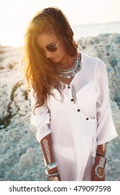 Beautiful boho styled girl wearing white shirt with fashion ethnic jewelery and flash tattoo at the beach in sunlight