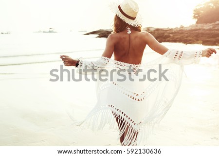 Beautiful boho styled model wearing white crochet swimsuit posing on the beach in sunlight