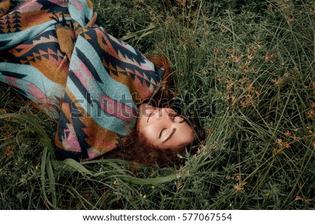Beautiful boho woman wearing poncho sitting on green field