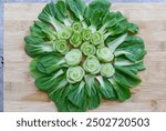 Beautiful bok choy vegetable arranged in a circle, like a flower on a wooden cutting board, The cut stalks from the center, while the green leaves fan outwards, creating a visually appealing design