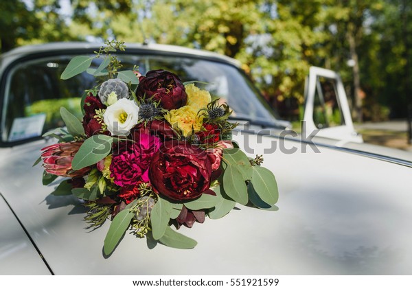 beautiful bouquet of burgundy flowers and green\
leaves lying on car