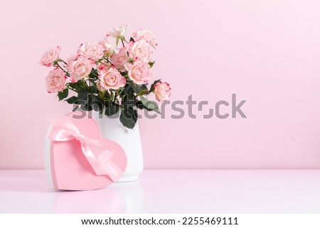 Beautiful bouquet flowers pink roses in vase and  gift box with satin bow on pastel pink background table. Birthday, Wedding, Mother's Day, Valentine's day, Women's Day. Front view