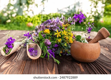 A beautiful bouquet of fresh herbs and flowers, including purple, yellow, and white blooms, lies on a rustic wooden table. Two wooden scoops hold smaller bundles of flowers, while a mortar and pestle  - Powered by Shutterstock