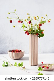 Beautiful bouquet of fresh wild strawberries with red, green berries and leaves in a vase, bowls. Healthy organic food concept.