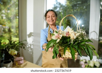 Beautiful bouquet of orchid flowers arranged in wicker basket, in the hands of blurred smiling florist, for festive life event. Flower arrangement with fresh orchids, gypsophila flower and palm leaves - Powered by Shutterstock