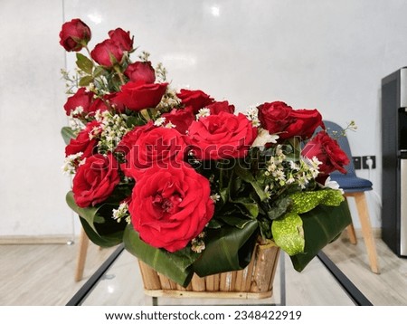 A beautiful bouquet of red roses and white daisies in a bamboo basket put on a long glass table. Used for the background