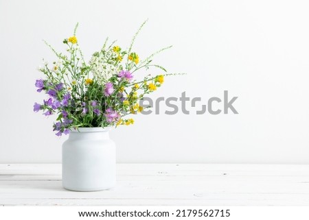 Beautiful bouquet of wild summer flowers in vase against white wall. 