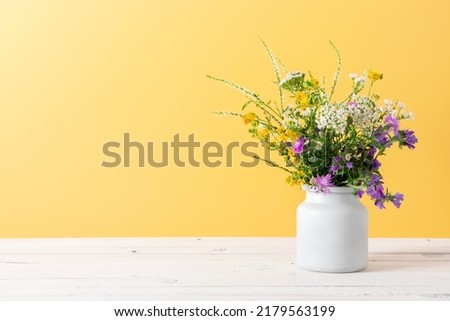 Beautiful bouquet of wild summer flowers in vase against yellow wall. 