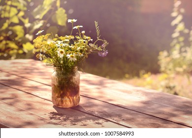 Beautiful bouquet of wildflowers on wooden table in garden. Vintage art photo of chamomile, cornflower and bell in yard decor.