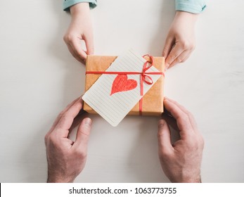 Beautiful box and gift  red ribbon  card and heart  loving father's hands   the youngest daughter white background  View from above  Preparation for Father's Day