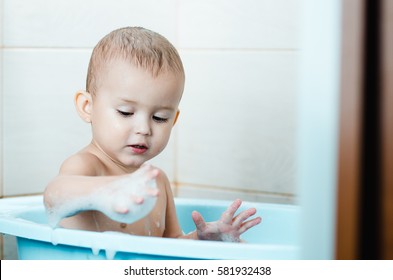 Beautiful boy bathing a toddler in the tub clean and hygienic,looks at the hand which in the foam