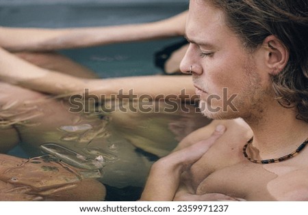 Beautiful boy with closed eyes bathing in the cold water among ice cubes in a plastic tank in a garden. Wim Hof Method, cold therapy, breathing techniques, yoga and meditation