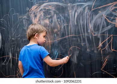Beautiful boy drawing on a blackboard, young artist