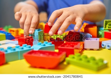 A beautiful boy is playing at home with building blocks. A cute smiling boy is playing with a constructor with a lot of colorful plastic blocks in the room, building a city. Preschool classes.