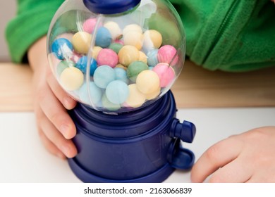 Beautiful boy plays with candy machine. Gumball Machine toy with colorful balls. Sweet childhood dream. Reward for good job done.