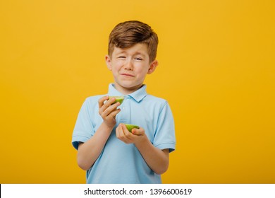 beautiful boy taste a fresh lime taste sour grimace, facial emotions negative, in blue T-shirt, isolated yellow background, copy space
