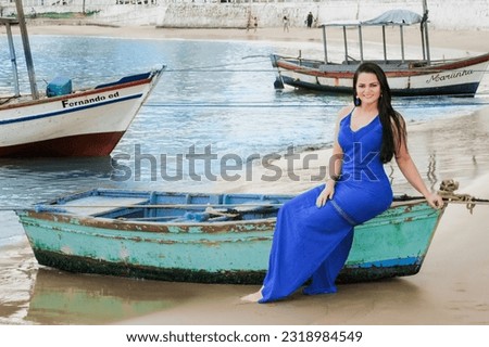 Beautiful Brazilian brunette woman in long dress on the beach with boats