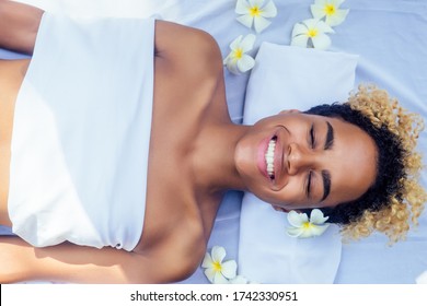 beautiful brazilian smiling girl lying on table with towel and white flowers ,massaging and pampering herself in luxury resort spa centre in Bali
