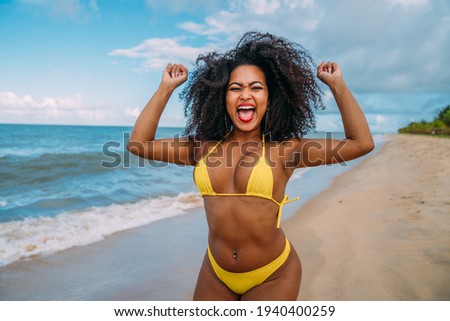 beautiful Brazilian woman in bikini on the beach. Young woman enjoying her summer vacation on a sunny day, smiling and celebrating looking at the camera