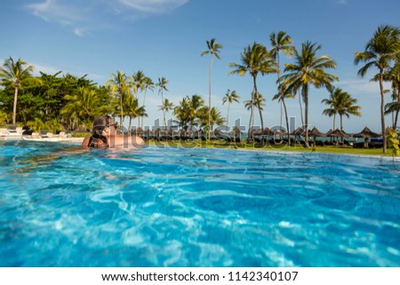 Beautiful brazilian woman enjoying vacation holidays at luxurious beachfront hotel resort with swimming pool and tropical lansdcape near the beach