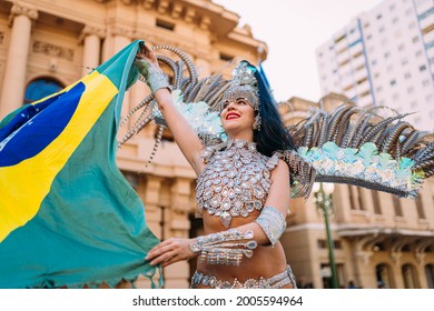 Beautiful Brazilian woman wearing colorful Carnival costume and Brazil flag during Carnaval street parade in city.