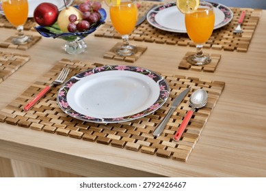 Beautiful breakfast table setup featuring fresh orange juice with lemon slices, a vibrant fruit bowl filled with apples, pears, and grapes, elegant plates, and rustic wooden placemats. Perfect for home decor and dining inspiration.