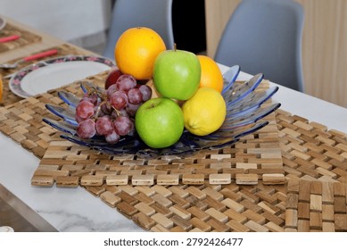 Beautiful breakfast table setup featuring fresh orange juice with lemon slices, a vibrant fruit bowl filled with apples, pears, and grapes, elegant plates, and rustic wooden placemats. Perfect for home decor and dining inspiration.