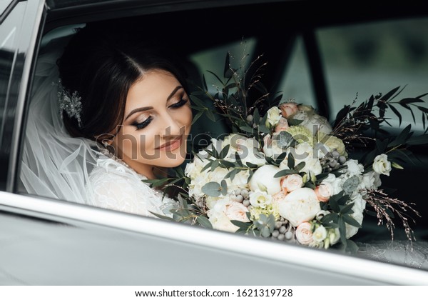 Beautiful bride with a bouquet in her hands\
sitting in a car near the window, reflection of the groom\'s\
silhouette. Wedding portrait of a cute blonde girl with flowers.\
Photography and\
concept.\
\
