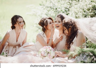 Schöne Braut und Brautjungfern sitzen auf dem Rasen