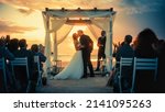 Beautiful Bride and Groom During an Outdoors Wedding Ceremony on an Ocean Beach at Sunset. Perfect Venue for Romantic Couple to Get Married, Exchange Rings, Kiss and Share Celebrations with Friends.