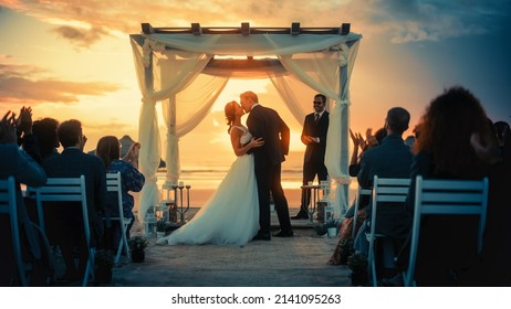 Hermosa novia y Groom durante una ceremonia de boda al aire libre en una playa del océano al atardecer. Lugar perfecto para que una pareja romántica se case, intercambie anillos, besos y comparta celebraciones con sus amigos.