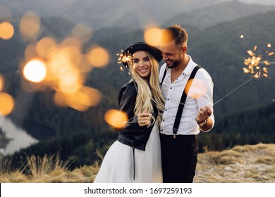 Beautiful bride and groom with sparklers on the top of the mountain. Wedding photoshoot. Smiling groom and bride. Blonde bride in black jacket . - Powered by Shutterstock