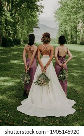 Beautiful bride and her bridesmaids standing on green field with their beck with flowers in hands.