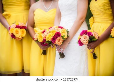 Beautiful Bride Holding Red, Yellow, Orange Bouquet With Bridesmaids In The Background.