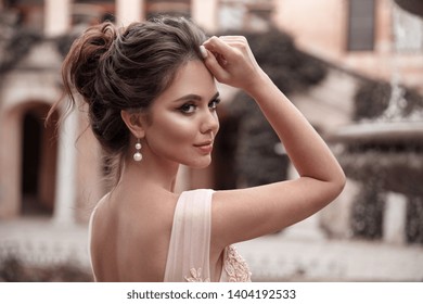 Beautiful bride with pearl earrings jewelry wears pink prom dress. Outdoor romantic portrait  of Attractive brunette woman with makeup and wedding  hair style posing at park. - Shutterstock ID 1404192533